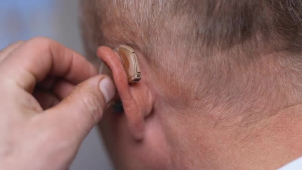 補聴器をつけてる。難聴の症状を持つシニア男性。成熟した耳の近くに指で男を緊張.補聴器を持った男. — ストック動画