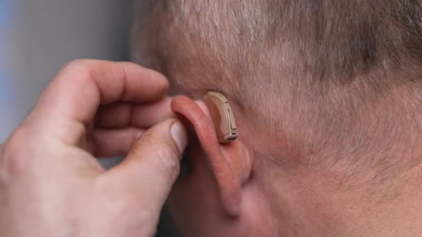 Крупным планом мужчина вставляет слуховой аппарат ей в ухо. Старик пользуется слуховыми аппаратами. Пожилой человек вставляет слуховой аппарат в левое ухо. Старший мужчина с симптомом потери слуха — стоковое видео