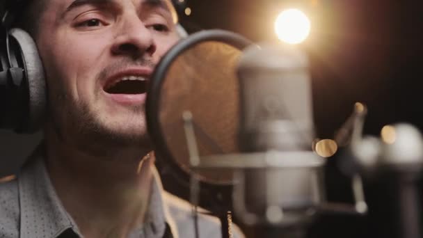 Ritratto giovane cantante con le cuffie, che canta in studio di registrazione. Maschio caucasico registra nuova traccia musicale, canta canzone in microfono. Processo di registrazione della canzone in studio di registrazione — Video Stock