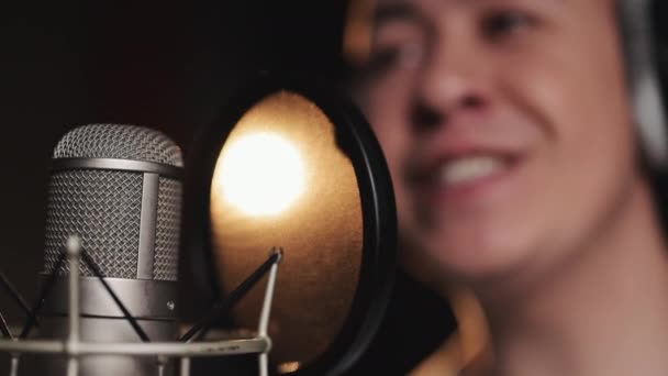Kulaklık takan genç profesyonel erkek şarkıcının kapanışı bir müzik stüdyosunda mikrofonla yeni bir şarkı söylüyor. — Stok video