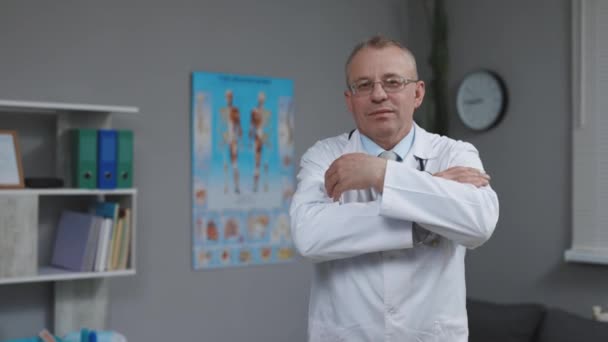 Självsäkra tankeväckande äldre vuxen man professionell sjukvårdare, gammal doktor bär vit medicinsk Coat glasögon håller stetoskop tittar på kameran på sjukhuset kontor. Begreppet hälso- och sjukvård och medicin — Stockvideo