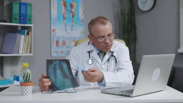Oudere Doctor Praten met Patiënt maken van Video Call op Laptop. Senior mannelijke arts spreken op zoek naar pc scherm communiceren door webcam in web chat consulting client online — Stockvideo
