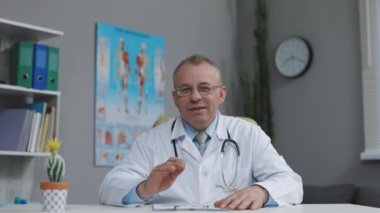 Orta yaşlı doktor kamerayla konuşuyor. İnternetten danışman hasta arıyor. Üst düzey GPS konferans sohbetinde konuşan web kamerasına bakıyor. Webcam yüz görüntüsü. Teletıp, tele sağlık danışmanlığı.