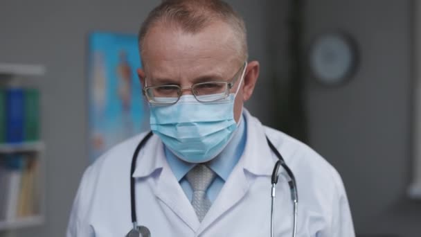 Close Up Ritratto di medico di famiglia in occhiali e maschera facciale. Medico di successo in camice bianco guarda la fotocamera in ufficio ospedaliero. Covid-19 Concetto pandemico di virus infettivo — Video Stock