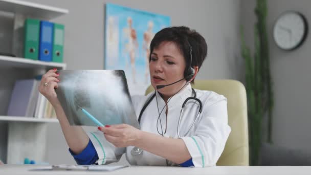Γυναίκα γιατρός σε λευκό ιατρικό παλτό και ακουστικά κάνοντας κλήση διάσκεψης στον υπολογιστή laptop, διαβούλευση απόσταση ασθενή σε απευθείας σύνδεση σε συνομιλία βίντεο, να εξηγήσει τη θεραπεία από την έννοια κάμερα — Αρχείο Βίντεο