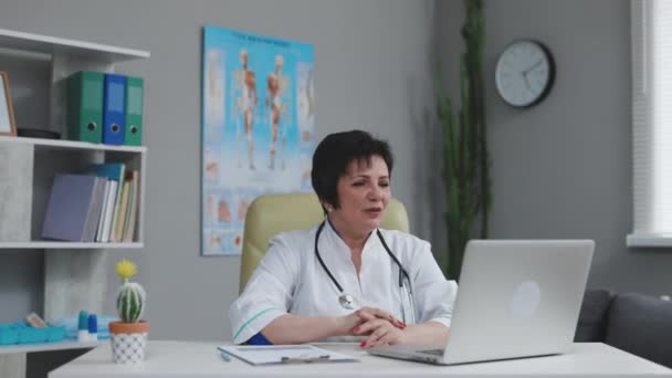 Lekarka nosi biały płaszcz, dzwoni do odległego pacjenta na laptopie. Lekarz rozmawiający z klientem za pomocą aplikacji wirtualnego czatu. Telemedycyna, koncepcja zdalnej opieki zdrowotnej — Wideo stockowe