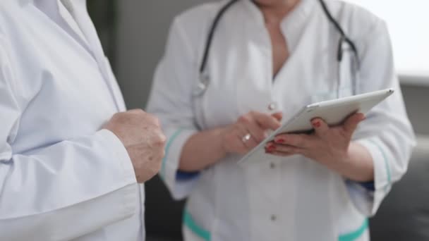 Vista de cerca de hombres y mujeres médicos que utilizan la tableta durante la jornada laboral en la clínica. Caucásico persona y sus colegas femeninos utilizar dispositivo electrónico y trabajar juntos mientras de pie en el interior. — Vídeos de Stock