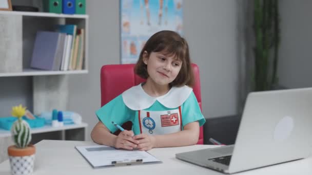 Happy cute small kid girl vlogger wear medical clothing talking to camera recording vlog for social media blog, video conference calling virtual friend having online meeting sitting on couch — Stock Video