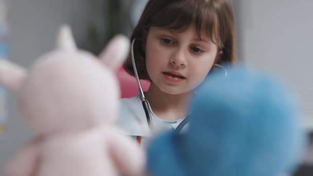 Söt söt liten förskola unge flicka bära medicinsk uniform hålla stetoskop lyssna sjuk leksak patient. Smart liten barn leker sjukhus spel som läkare låtsas sjuksköterska koncept. — Stockvideo