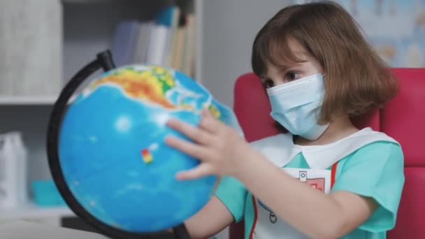Маленькая милая девочка-доктор надевает маску на земной шар планеты Земля. Спасите руки планеты Земля. Наше будущее в твоих руках. Маленькая девочка в костюме врача лечит планету Земля. — стоковое видео