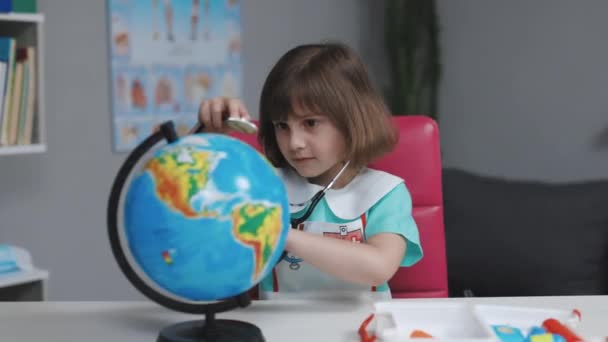 Dívka je oblečena v lékařských šatech se stetoskopem ve svých rukou zkoumá a hraje hru na léčení planety Země. Světová planeta Země je ekologická. Nemocná Země planeta Covid-19 příznaky. — Stock video