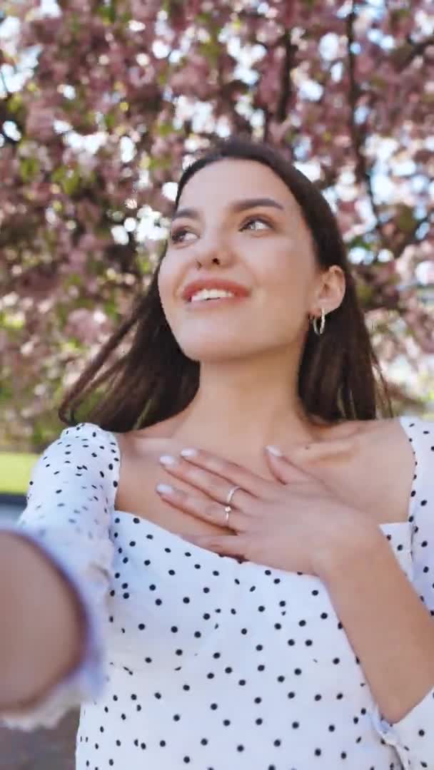Vertical video of smiling girl having video call on smartphone in city park, friendly woman waving hand at camera, pretty woman video chatting at phone, stylish blogger making video on phone outdoor — Stock Video