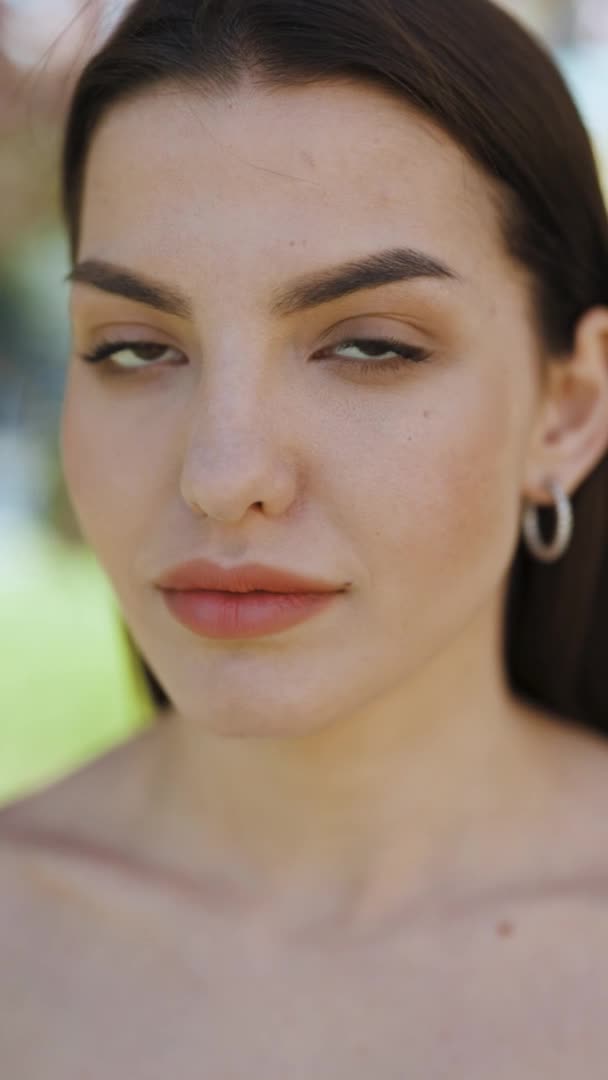 Vídeo en formato vertical Rostro de hermosa mujer suave con maquillaje natural mirando a la cámara. Retrato joven chica morena bonita fuera a la luz del sol. Etnnicidad. Gente. Belleza — Vídeos de Stock