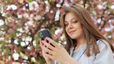 Gülümseyen kadın Central Park caddesinde yürüyor ve telefonunu kullanıyor. Güzel yaz kadını cep telefonuna bakıyor..