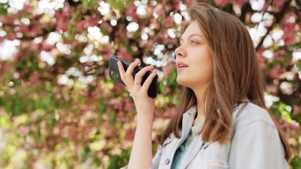 Happy girl using smart phone voice recognition, dictates thoughts, voice dialing message outdoor talking to mobile assistant. Talking mouth in the speaker of a young woman. — Stock Video