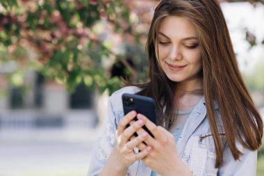 Akıllı telefon kullanan gülümseyen kadın. Sosyal medya uygulaması mesajları kullanan kız dışarıda gülümseyen haberler alıyor. İletişim, sosyal ağlar, online alışveriş konsepti. Teknoloji