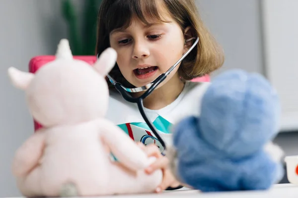 Niño jugando juego de hospital fingiendo ser médico, veterinario, médico tratar a los animales sin hogar. Niño linda niña preescolar con uniforme médico, escuchando a las mascotas respirar, loros y pacientes de juguete —  Fotos de Stock