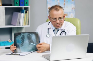 Yaşlı doktor laptopta video görüşmesi yapan hastayla konuşuyor. İnternet sohbet danışmanlığında web kamerasıyla iletişim kuran bilgisayar ekranına bakan kıdemli erkek doktor.