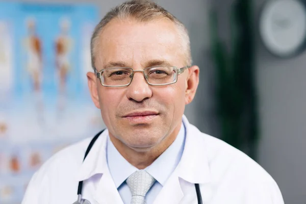 Retrato de médico de familia caucásica en gafas está en la Clínica de Salud. Médico exitoso en bata blanca de laboratorio mira a la cámara y sonríe en la oficina del hospital Imagen De Stock