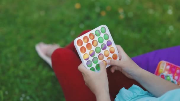 Renkli silikon anti-stres oyuncağı patlat. Gençler ve çocuklar için yeni bir moda. Doğada Popit oyuncağıyla oynayan bir kızın elleri. Çocukların elleri gökkuşağı oyuncağıyla oynar. — Stok video