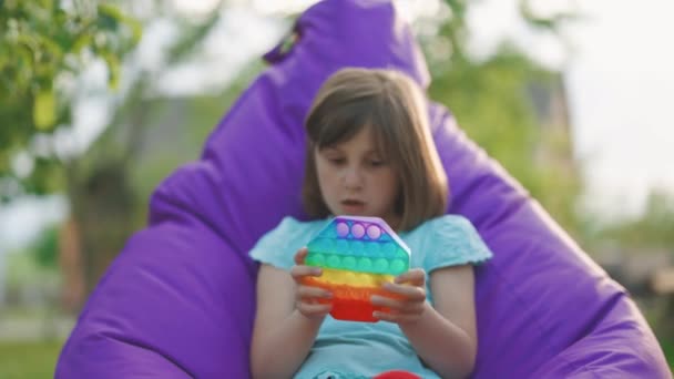 Menina apertando colorido brinquedo anti-stress. A criança está jogando um jogo popular com botões, um brinquedo anti-stress. Jogos educativos infantis. Abre. tela sensível ao toque anti-stress colorida — Vídeo de Stock