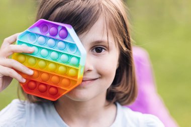 Küçük kızın portresini modern popit oyuncağıyla kapatın. Renkli ve parlak, basit bir gamzesi var. Son moda stres önleyici oyuncaklar itin ve çocukların eline basit gamzeler verin.