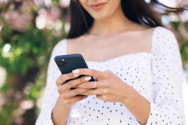 Kobieta w białej sukience za pomocą smartfona. Dziewczyna korzystająca z aplikacji social media SMS otrzymuje wiadomości uśmiechnięte na zewnątrz. Komunikacja, portale społecznościowe, koncepcja zakupów internetowych. Technologia — Zdjęcie stockowe