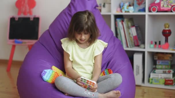 Menina está jogando pop-lo brinquedo. Colorido e brilhante pop-lo brinquedo. Um brinquedo útil para criança. Simples covinha. Criança segurando a pressão de silicone na moda aliviando o pop sensorial brinquedo — Vídeo de Stock