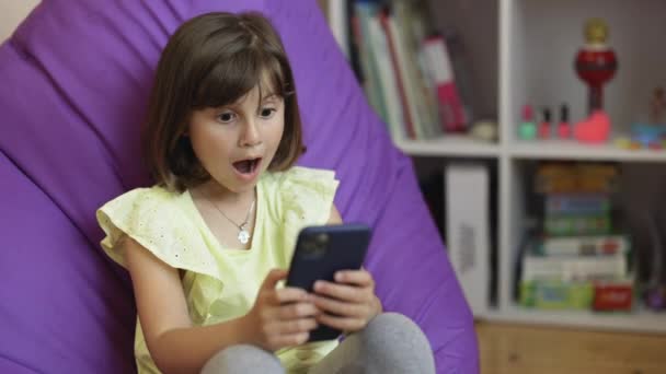 Petit enfant apprendre dans le téléphone portable, regarder la vidéo, s'amuser avec le concept de technologie mobile. Jeune fille mignonne tenant téléphone intelligent profiter de l'utilisation d'applications mobiles, jouer à des jeux à la maison — Video