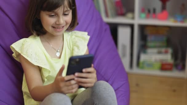 Nettes Kindermädchen hält Telefon, Kind nutzt Smartphone, Kind surft im Internet, verwendet Videokommunikation zu Hause am Telefon — Stockvideo