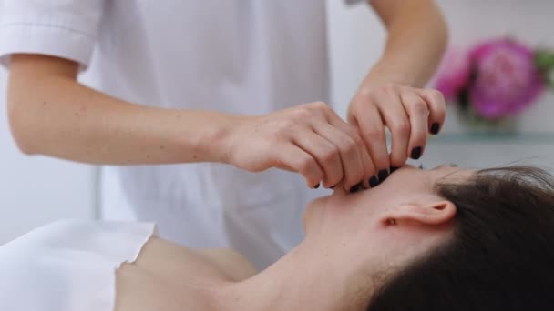 Ręczny masaż twarzy dla młodej kobiety w klinice kosmetycznej. Akcja. Masaż terapeuta pracuje na kobiecej twarzy, koncepcja relaksu — Wideo stockowe