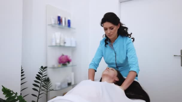 Mulher nova que tem massagem por um massagista feminino no pijama médico azul no centro de saúde moderno. Conceito de bem-estar. Mulher relaxante durante a massagem deitada na mesa de massagem — Vídeo de Stock