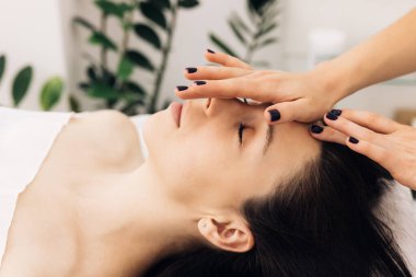 Spa yatağında yatan kadın güzellik salonundaki masaj terapistinden aroma yağı cildiyle yüz masajı yaptırıyor. Sağlık vücut masajı ve yüz spa konsepti.