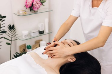 Sağlık, stres atma ve gençleştirme konsepti. Masaj terapistinin lüks bir spa merkezinde yüz masajı ve spa tedavisi için kaplıcaya uzanmış rahat bir kadın.