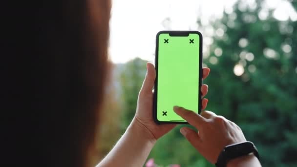 Πίσω Όψη της γυναίκας Brunette κρατώντας Chroma κλειδί πράσινη οθόνη Smartphone Watching Περιεχόμενο χωρίς να αγγίξετε ή να Swiping. Κορίτσι που χρησιμοποιεί το κινητό τηλέφωνο, Περιήγηση στο Internet, Watching Content — Αρχείο Βίντεο