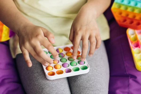 Stressful person playing with Popit push pop bubble fidget toy. Topview of playing a popular anti-stress toy game. Childrens hands play with the rainbow pop it fidget toy — Stock Photo, Image