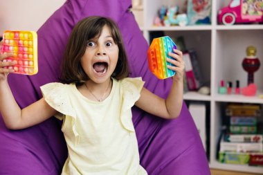 Küçük kız pop it basit snapperz oyuncağı oynuyor. Renkli ve parlak bir oyuncak. Çocuk için yararlı bir oyuncak. Basit bir gamze. Moda silikon basınçlı çocuk rahatlatıcı duyusal patlayıcı oyuncak