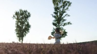 Elinde şapkası olan mutlu bir kız kolları açık lavanta tarlasında koşuyor. Kadınlar kırsal kesimde temiz havanın tadını çıkarırlar. Mutlu kız tarlada mor lavanta çiçekleriyle koşar.