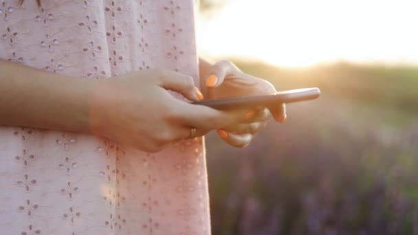 Χέρι του κοριτσιού χρησιμοποιώντας το μήνυμα πληκτρολόγησης smartphone. Γυναίκα δακτυλογράφηση από κινητό τηλέφωνο σε εξωτερικούς χώρους. Κοντινό πλάνο χαρούμενο κορίτσι με τα πόδια με smartphone στο αστικό υπόβαθρο. Η κυρία κρατάει το κινητό απ 'έξω. — Αρχείο Βίντεο