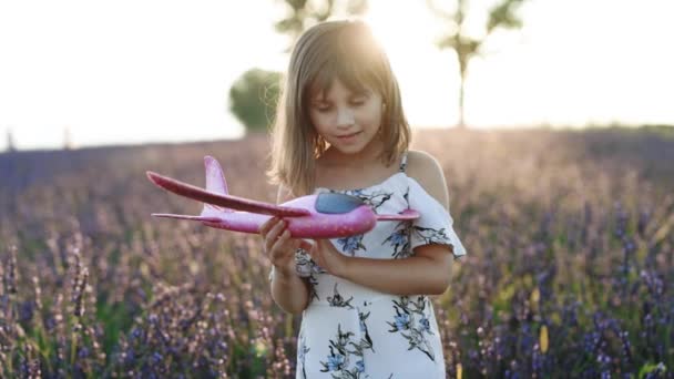 Criança feliz brincando com avião de brinquedo contra fundo céu de verão. Menina jogando avião em um campo de lavanda de verão. Melhor conceito de infância. Close up retrato de jovem menina feliz com avião. — Vídeo de Stock