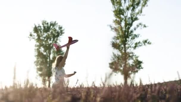 Glad liten flicka leker med flygplan på ett lavendelfält under solnedgången. Barn leker leksaksflygplan. Flickan vill bli pilot och astronaut. Begreppet stora barn dröm — Stockvideo
