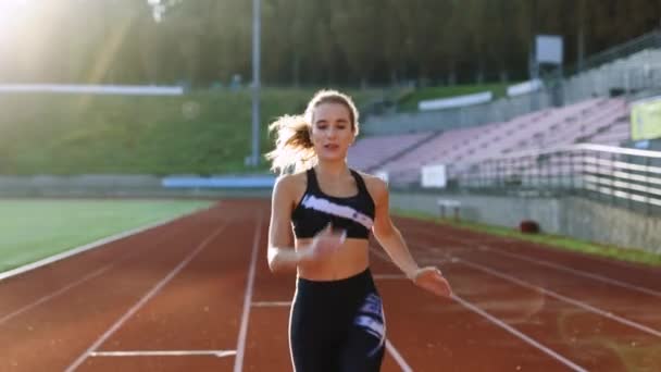 Front view of running caucasian woman in black sportswear doing cardio workout on sports track of stadium. Adult female athlete jogging, training before marathon competition. Health. Sportswoman. — Stock Video