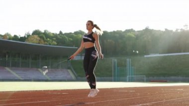 İple atlayan bayan sporcu. Alımlı bir kadın antrenman rutininin bir parçası olarak stadyumun spor pistinde ip atlıyor, kararlı bir kadın spor hedeflerine ulaşmaya odaklanıyor.
