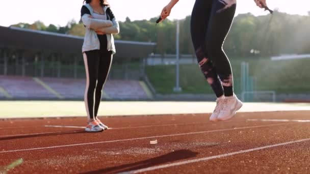 Primer plano de la atlética mujer caucásica con entrenador personal saltando la cuerda como parte de su entrenamiento de fitness. Deportiva hembra con una buena figura salta cuerda en pista deportiva del estadio — Vídeo de stock