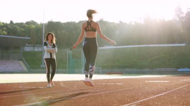 Spor salonunun bir parçası olarak kişisel antrenörüyle ip atlayan beyaz bir kadın. Güzel vücutlu, sportif bir kadın stadyumun spor pistinde ip atlıyor. Güç ve kardiyo egzersizi.