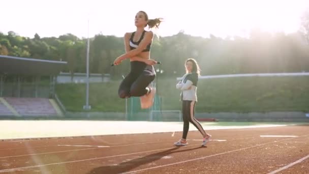 Atletische vrouw met persoonlijke instructeur springtouw als onderdeel van haar fitnesstraining. Sportieve vrouw met een goed figuur springt touw op de sportbaan van het stadion. Krachttraining cardio- en krachttraining — Stockvideo