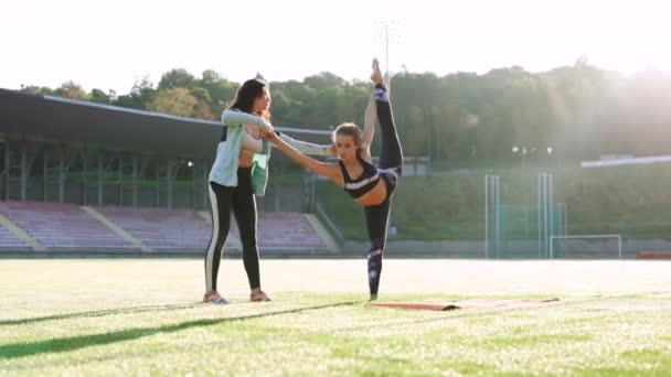 Atletische vrouw die yoga poseert bij zonsopgang. Fitness onderwijs yoga van mensen. Vrouw die yoga beoefent met personal trainer buiten in zonnige dag. Meisje dat yoga beoefent met trainer — Stockvideo