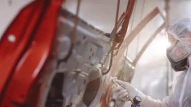 Oto boyacısı özel kabinde arabanın kapısına kırmızı boya sıkıyor. Araba servisi atölyesinde araç parçaları boyuyorum. Erkek teknisyen hava boyalı araba kapısı. Endüstriyel sprey boya işlemi