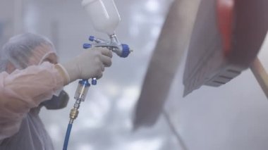 Araba servisi atölyesinde araç parçaları boyuyorum. Araba üretim fabrikası. Otomobil boyacısı özel bölmede arabanın kapısına kırmızı boya sıkıyor.