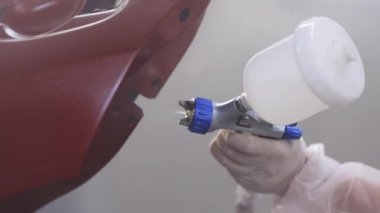 Ressam garajda kırmızı arabayı boyar. Profesyonel sprey silahla araba boyama. Usta araba servisinde otomobilin bir parçasını boyuyor.